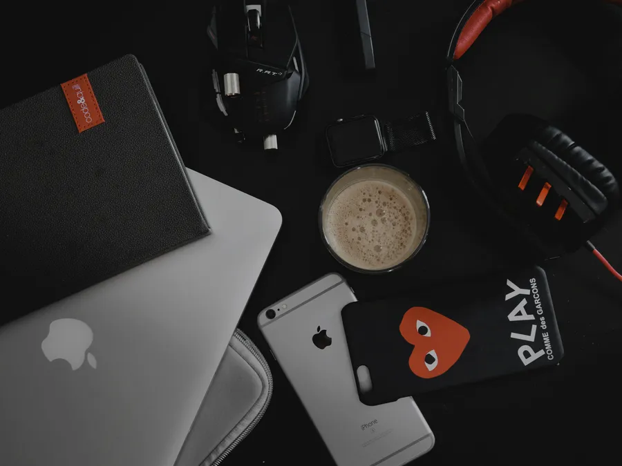 A laptop, phone, headphones, and charging cables laid out on a desk